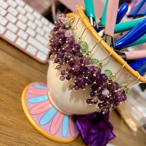 May include: Three pairs of dangle earrings with amethyst and green glass beads, shaped like bunches of grapes, hanging from gold-toned hooks.