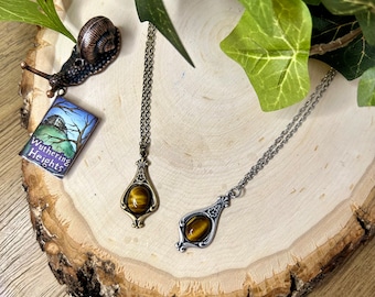 May include: Two necklaces with tiger's eye pendants. The pendant on the left is on a gold chain and the pendant on the right is on a silver chain. Both pendants are in an ornate, vintage style.