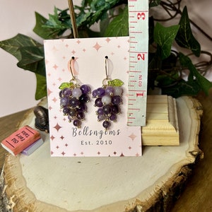 May include: Amethyst grape earrings with gold wire and green leaves. The earrings are displayed on a white card with the text "Bellsngems Est. 2010".