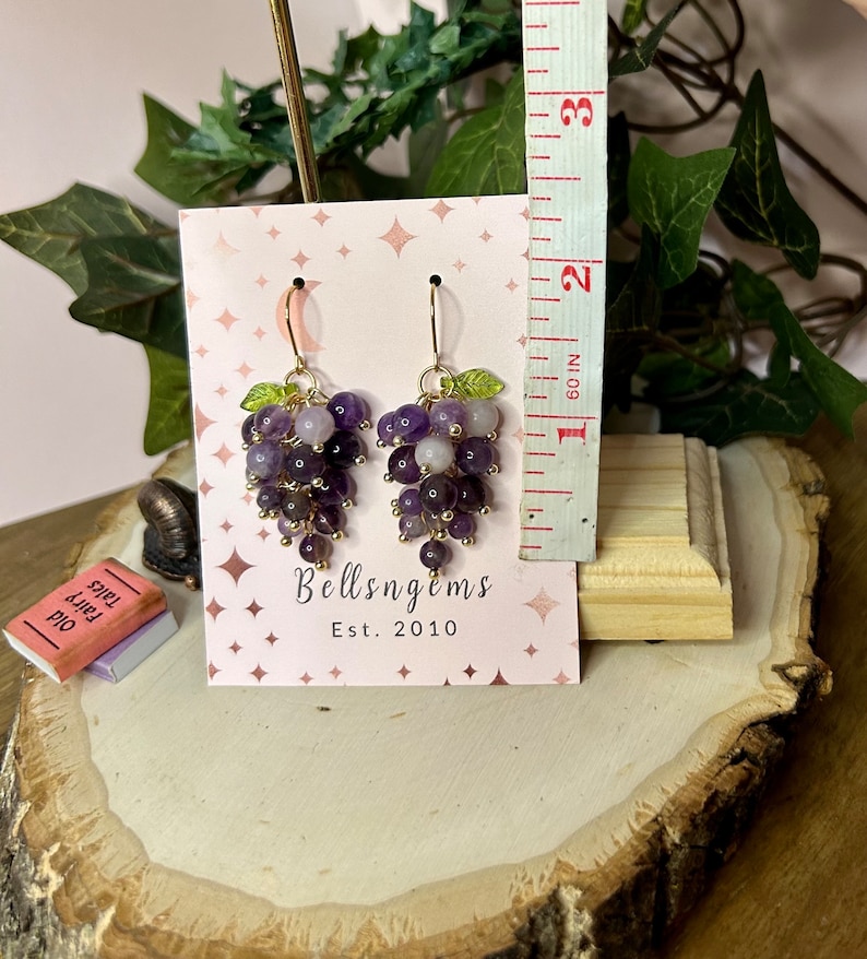 May include: Amethyst grape earrings with gold wire and green leaves. The earrings are displayed on a white card with the text "Bellsngems Est. 2010".