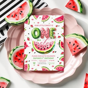 Puede incluir: Un plato rosa con borde festoneado contiene una invitación con temática de sandía para un primer cumpleaños. La invitación presenta el texto "ONE in a melon" e ilustraciones de rodajas de sandía. Decoraciones en forma de sandía rodean el plato.