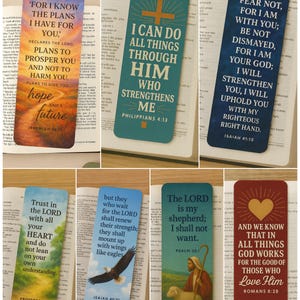 May include: A collection of colorful bookmarks with inspirational quotes from the Bible. Each bookmark features a unique design with text from Jeremiah, Philippians, Isaiah, Proverbs, Psalm, and Romans. The bookmarks are rectangular and rest on open books.