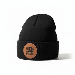 May include: Black knit beanie with a brown leather patch. The patch features a graphic of a truck with the text "SHE WANTS THE DIESEL". The beanie is a classic style, suitable for cold weather.