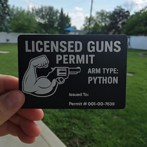 May include: Black rectangular card with the words "LICENSED GUNS PERMIT" in white. The card features a graphic of a flexing arm holding a handgun, with the text "ARM TYPE: PYTHON". The permit number is 001-00-7639.