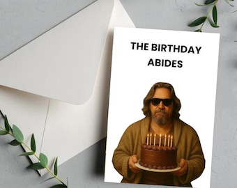 May include: A birthday card with the text "THE BIRTHDAY ABIDES" and an image of a man holding a chocolate cake with lit candles. The card is inside a white envelope, with a sprig of greenery in the background.