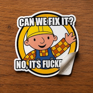 May include: A sticker featuring a cartoon construction worker in a yellow hard hat and blue overalls. The sticker has the text "CAN WE FIX IT?" above the character and "NO, IT'S FUCKED" below. The sticker is on a wooden surface.