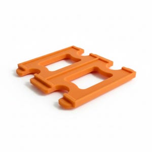 May include: An orange plastic interlocking building block, featuring a rectangular shape with two open rectangular spaces and notched edges. The block is designed to connect with other similar blocks, creating larger structures.