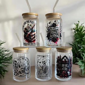 May include: Five clear glass drinking jars with bamboo lids and glass straws. Each jar features a different black and red graphic design with text. The designs include books, roses, and skulls. The text includes phrases like "Trigger Warning" and "Good Girls Read Bad Books."