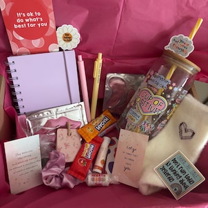 Peut inclure: Une boîte cadeau rose remplie d'articles de bien-être. Comprend un carnet, des stylos, un gobelet avec une paille, des collations, un baume à lèvres et des cartes avec des citations inspirantes. La boîte est doublée de papier de soie rose.