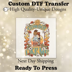 May include: A DTF transfer featuring a graphic illustration of two figures in cowboy hats and boots, one in a dress and one in cow-print pants, standing under a sun and floral arch with the text "COWBOY LIKE ME" in blue and orange lettering.
