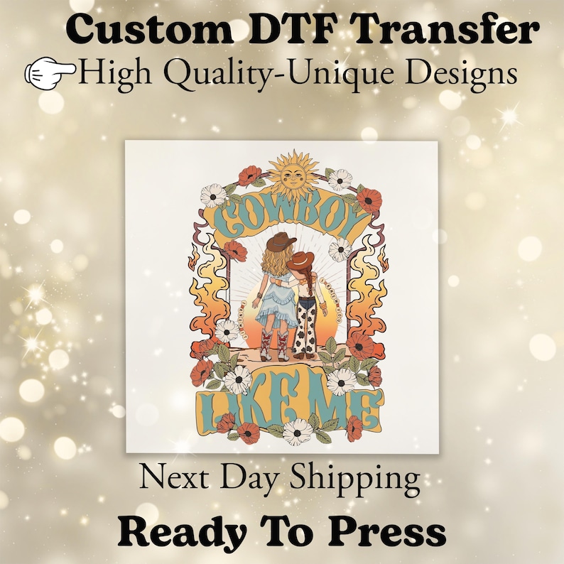 May include: A DTF transfer featuring a graphic illustration of two figures in cowboy hats and boots, one in a dress and one in cow-print pants, standing under a sun and floral arch with the text "COWBOY LIKE ME" in blue and orange lettering.