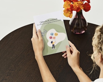 Peut inclure: Un cahier avec le texte "Calme-toi & continue!" et "Un cahier sur la régulation émotionnelle" est tenu par une personne. La couverture présente une illustration de dessin animé d'une personne tenant des ballons avec différentes expressions faciales. Un vase de fleurs oranges est en arrière-plan.