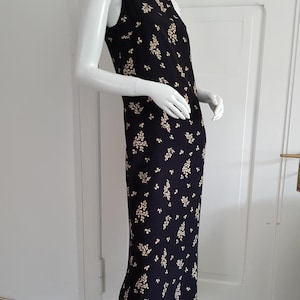 May include: A sleeveless midi dress with a black background and a white floral pattern. The dress has a scoop neck and a fitted silhouette.