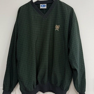 May include: A dark green and black plaid V-neck pullover sweater. The sweater has a black collar, cuffs, and hem. A small embroidered emblem is on the upper left chest. The sweater is hanging on a white hanger.
