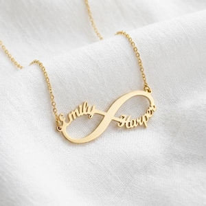 Könnte beinhalten: Eine goldfarbene Metallhalskette mit einem Unendlichkeitssymbol als Anhänger. Der Name Emily ist in die linke Schlaufe des Unendlichkeitssymbols integriert, während der Name Harper in die rechte Schlaufe eingearbeitet ist. Der Anhänger hängt an einer feinen Goldkette.