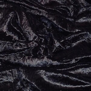 May include: Close-up of a black velvet fabric with a shimmering, textured surface. The fabric is draped, creating folds and shadows that highlight its luxurious appearance. The dark color and sheen suggest a formal or elegant textile.