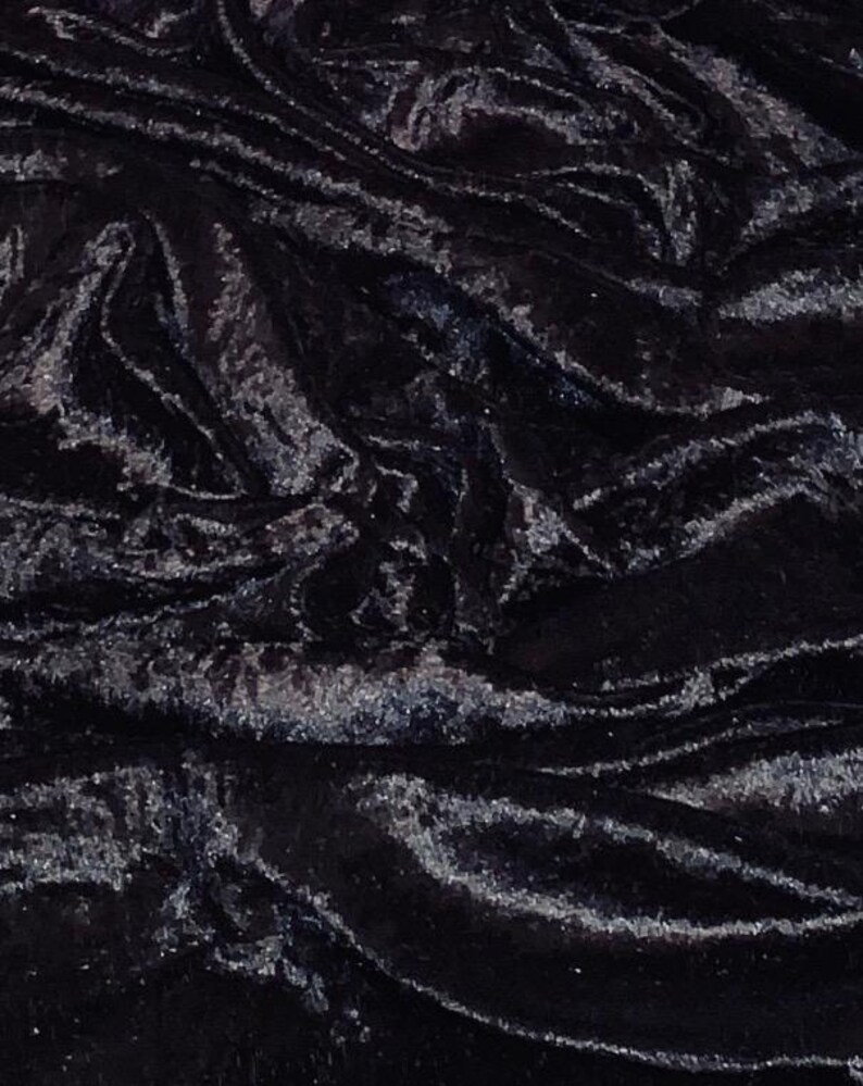 May include: Close-up of a black velvet fabric with a shimmering, textured surface. The fabric is draped, creating folds and shadows that highlight its luxurious appearance. The dark color and sheen suggest a formal or elegant textile.