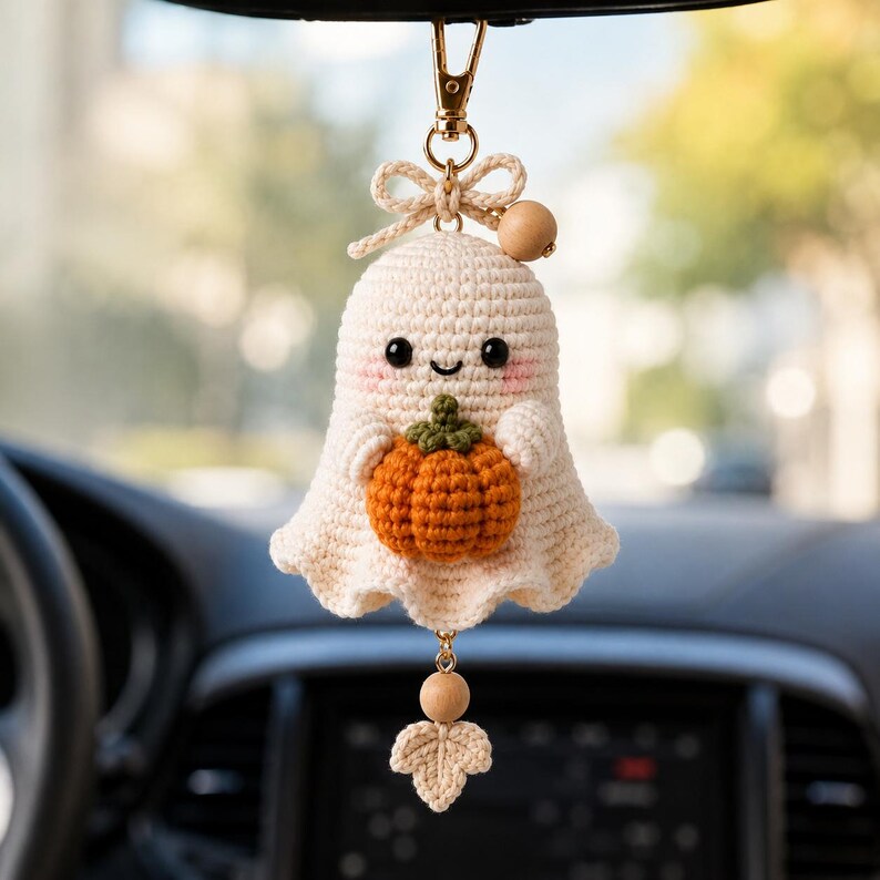 Peut inclure: Un ornement fant&ocirc;me crochet&eacute; de couleur cr&egrave;me tenant une petite citrouille orange avec une tige verte dans ses bras. Le fant&ocirc;me a des yeux en perles noires, un sourire brod&eacute; et des joues roses. Il est suspendu &agrave; un fermoir dor&eacute; avec une perle en bois.