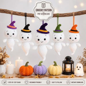 May include: Five crocheted white ghosts with smiling faces and colorful hats hang from a branch. Below are three crocheted pumpkins in orange, purple, and yellow, a black metal lantern with a lit candle, and a small white ghost-shaped light.