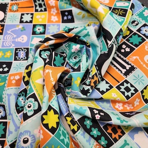May include: A fabric featuring a grid pattern of squares in orange, light blue, yellow, and black. The squares contain illustrations of skeletons, bones, spiders, and flowers. The material is gathered in the center, creating folds and shadows.