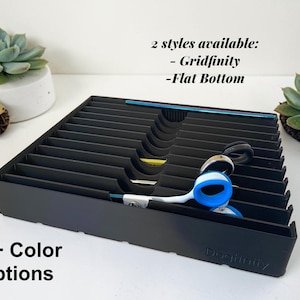 May include: A black rectangular organizer tray with multiple parallel slots and curved cutouts for tool storage. The tray features the embossed text Dogfinity and includes the printed text 2 styles available: - Gridfinity - Flat Bottom and 50+ Color Options.