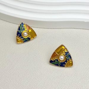 May include: A pair of gold-coloured triangle earrings with colourful enamel detailing. Each earring features a central faux pearl and a geometric design with blue, green, orange, and yellow accents. The earrings have a post back.