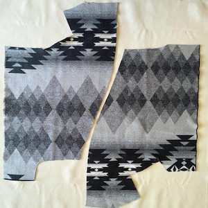 May include: Two pieces of fabric with a gray, black, and white geometric pattern. The design features diamond shapes and stylized tribal motifs. The fabric pieces are cut in a shape that suggests they are for a garment.