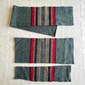 May include: Three pieces of green fabric with red, blue, and yellow stripes. The fabric is cut into different lengths.