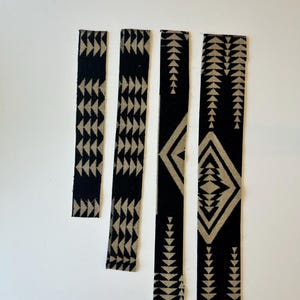 May include: Four rectangular fabric strips arranged vertically, featuring a black background with a repeating beige geometric pattern of triangles and diamonds. The strips vary in length and width, displaying a consistent woven-style textile design.