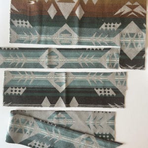May include: Four rectangular strips of woven fabric featuring a geometric pattern in shades of teal, grey, brown, and cream. The design includes repeating diamond shapes, arrow motifs, and horizontal bands with a soft, textured appearance.
