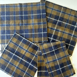 May include: A collection of four rectangular scarves featuring a plaid pattern in shades of olive green and navy blue, accented with thin white intersecting lines. Each scarf is finished with short, fringed edges along the bottom hem.