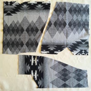May include: Four pieces of fabric with a geometric pattern in shades of gray and black. The design features diamond and triangular shapes, creating a Southwestern or tribal aesthetic. The fabric pieces are cut in various shapes, suggesting they are for a sewing project.