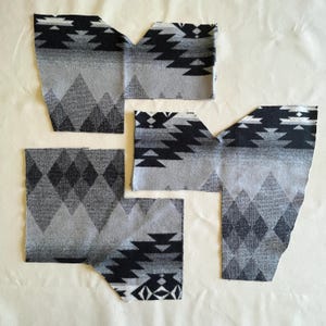 May include: Five pieces of fabric with a Southwestern pattern in shades of gray and black. The fabric pieces are cut into various shapes, including diamond and geometric designs. The fabric is laid out on a light-colored surface.
