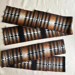 May include: Four pieces of fabric with a geometric pattern in shades of brown, black, and white. The design features repeating triangular shapes. The fabric pieces are arranged on a light-colored surface, showcasing the intricate pattern and color variations.