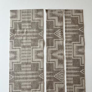 May include: Three rectangular fabric strips featuring a repeating geometric pattern in shades of taupe and cream. The design consists of interlocking stepped lines and triangular motifs arranged in a symmetrical, repeating layout across the surface.