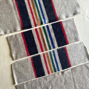 May include: Three rectangular gray fabric pieces with colorful striped patterns. Each piece has a central stripe of navy blue, red, orange, green, and blue. The edges are gray with a white seam.