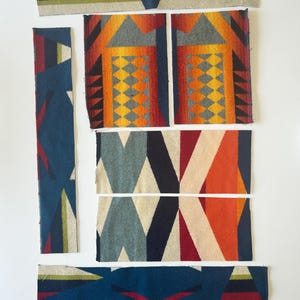 May include: Assortment of colorful woven fabric pieces. The pieces feature geometric patterns in shades of blue, red, orange, yellow, and gray. The designs include triangles, diamonds, and rectangular shapes. The fabric appears to be a wool blend.