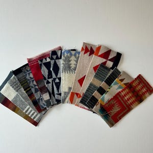 May include: A collection of rectangular fabric swatches arranged in a fan shape. Each swatch features distinct woven patterns including geometric shapes, stripes, and triangles in various colors such as red, blue, black, grey, and tan.