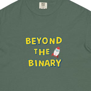 May include: A dark green t-shirt with the text "BEYOND THE BINARY" in yellow, along with a cartoon rocket ship graphic. The shirt is a short-sleeved, crew neck style.