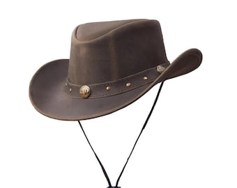 Könnte beinhalten: Brauner Cowboyhut aus Leder mit breiter Krempe und hohem Oberteil. Der Hut hat dekorative Metallnieten und ein Medaillon am Hutband. Ein schwarzer Kinnriemen ist befestigt. Klassischer Western-Stil.