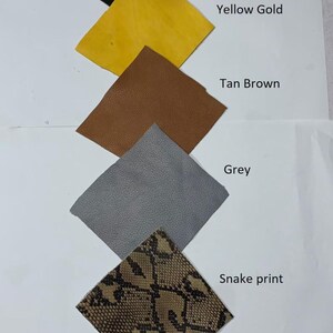 Pode incluir: Uma cole&ccedil;&atilde;o de amostras de couro em v&aacute;rias cores e texturas. As amostras incluem preto, amarelo dourado, castanho claro, cinza e uma estampa de cobra. Cada amostra &eacute; rotulada com o nome da cor ou padr&atilde;o.