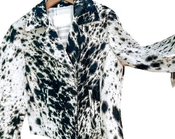 May include: A black and white spotted jacket with a classic collar and zipper closure. The jacket is hanging on a wooden hanger. The pattern resembles a cowhide print, offering a bold and unique style.