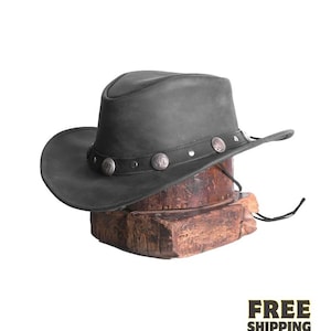 Könnte beinhalten: Ein dunkelgrauer Cowboyhut mit breiter Krempe und einem dekorativen Band mit silberfarbenen Verzierungen. Der Hut wird auf einem Holzblock präsentiert. Ein schwarzer Kinnriemen ist befestigt. Die Worte "FREE SHIPPING" stehen unten.