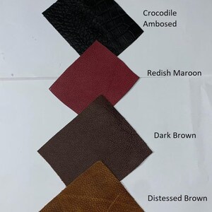 May include: A collection of leather swatches in various colors, including white, black with a crocodile embossed pattern, reddish maroon, dark brown, and distressed brown. Each swatch is labeled with its respective color name.