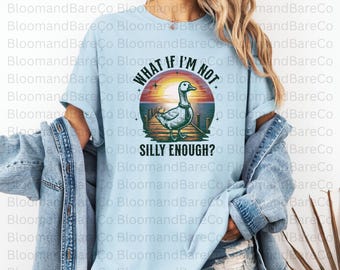 Op de afbeelding: Een lichtblauw T-shirt met een vintage-stijl afbeelding van een eend met een stropdas die op een dok staat. De afbeelding zegt "What if I'm not silly enough?"