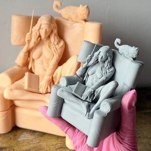 Könnte beinhalten: Hellgraue Figur einer Person, die in einem Stuhl sitzt und einen Zauberstab und ein Buch hält. Eine Katzenfigur sitzt auf der Stuhllehne. Eine weitere Pfirsichfigur befindet sich im Hintergrund. Die Figur wird von einer Person mit einem rosa Handschuh gehalten.