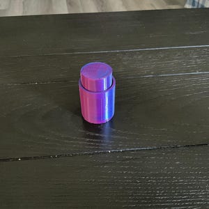 May include: A purple and blue iridescent bottle stopper. The stopper is made of two pieces, a top and a bottom, that fit together.