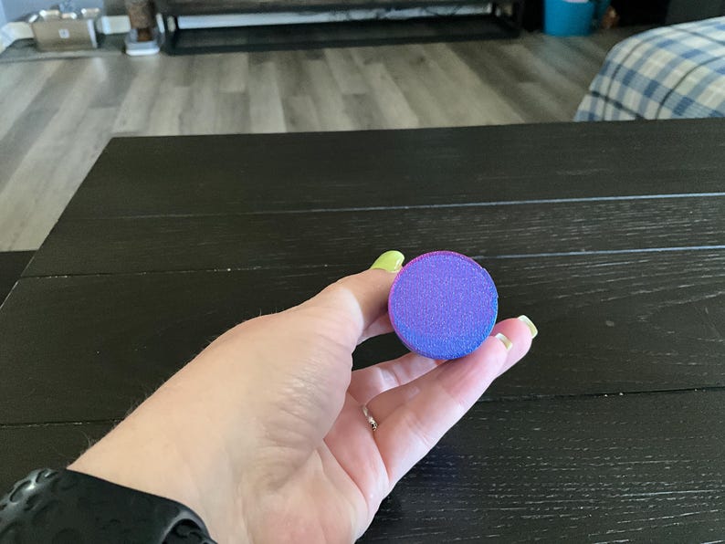 Puede incluir: Una esponja de maquillaje redonda, de color morado y rosa, con una superficie texturizada.
