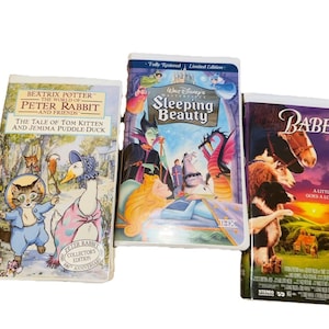 Puede incluir: Se muestran tres cintas de VHS. Una presenta el texto "BEATRIX POTTER THE WORLD OF PETER RABBIT AND FRIENDS" y "THE TALE OF TOM KITTEN AND JEMIMA PUDDLE DUCK". Otra es "Walt Disney's Sleeping Beauty". La tercera es la película "Babe".