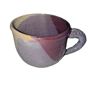 May include: A handmade ceramic mug with a unique, textured design. The mug features a color scheme of lavender, burgundy, and cream, with a twisted handle. The interior and rim are burgundy, while the exterior has a diagonal color block design.